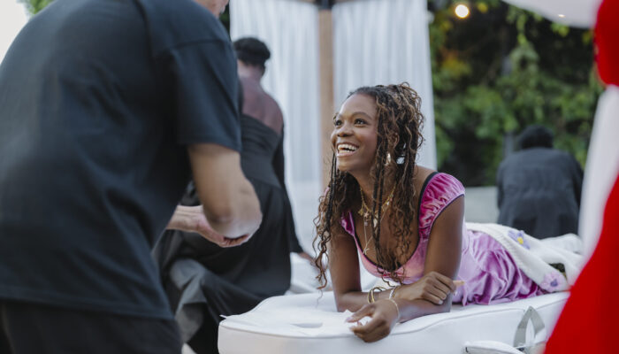 Woman smiling while lying on a massage table outdoors, engaging in conversation during a wellness event.