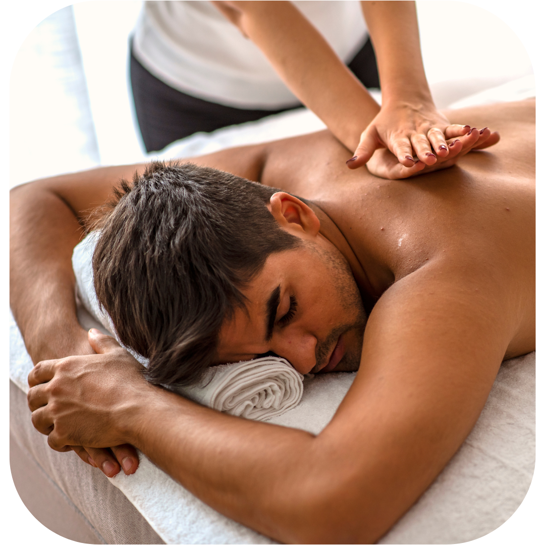 Male client lying face down on a massage table receiving Swedish massage, therapist applying gentle pressure with both hands to the back.