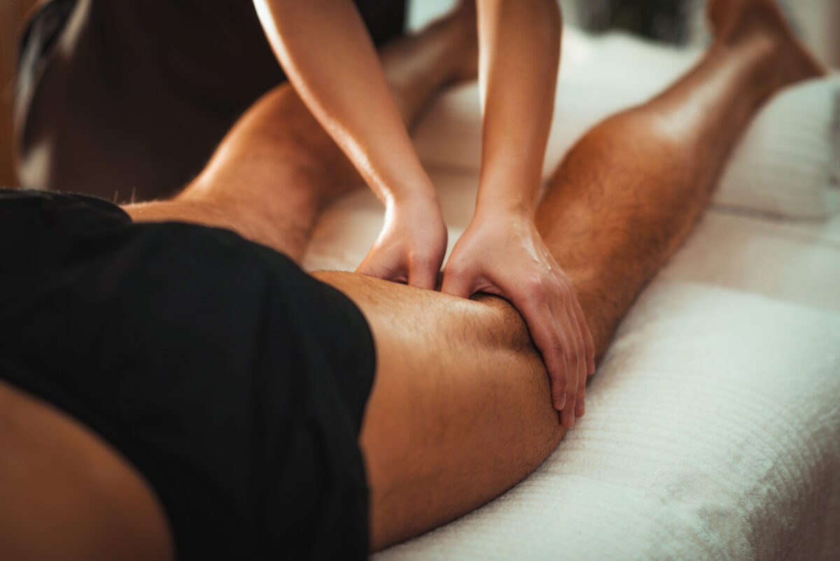 Therapist performing deep tissue massage on male athlete’s thigh to relieve muscle tension and aid recovery.