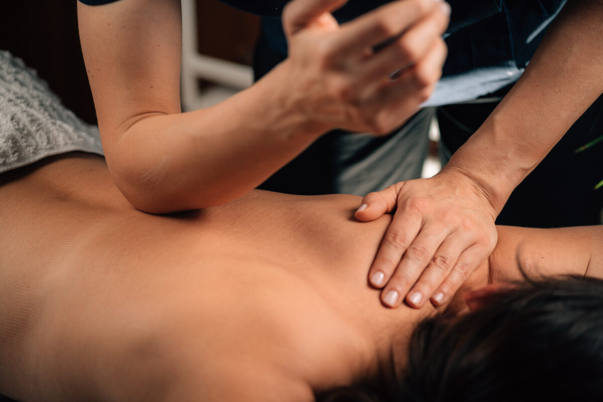 Massage therapist using elbow and hand pressure during a deep tissue massage on a client’s back.