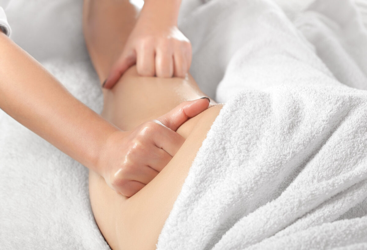 Massage therapist applying deep pressure to the hip and outer thigh area during a deep tissue massage for IT band pain.