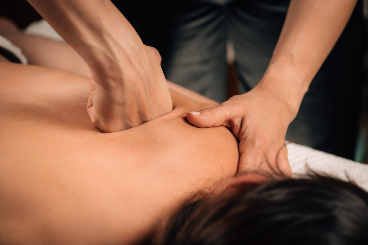 Close-up of a massage therapist applying deep tissue pressure to a client's shoulder muscles