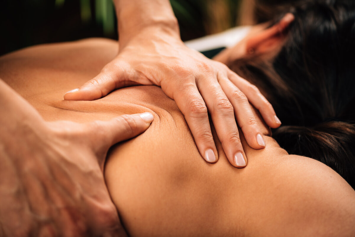 Massage therapist applying firm pressure to the upper back and shoulder area during a deep tissue massage.