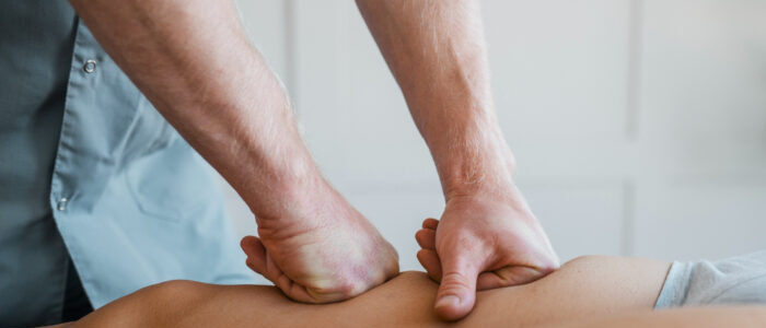 Massage therapist performing deep tissue massage using compression technique with both hands on a client’s leg.
