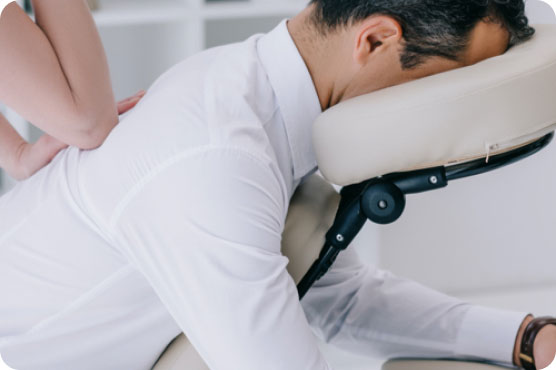 Massage therapist performing a seated chair massage on a man wearing a white dress shirt in an office setting.