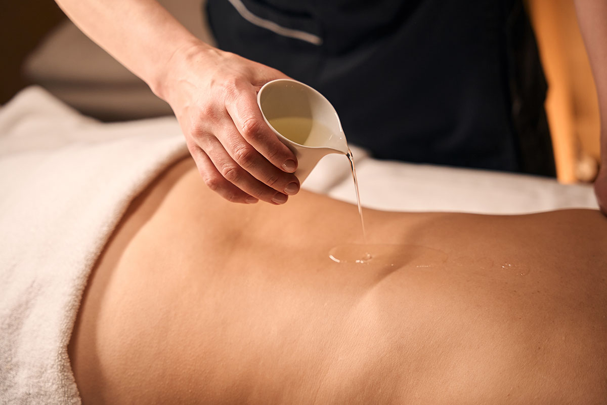 Close-up of a therapist pouring warm herbal oil onto a client’s back during an Ayurvedic massage session.