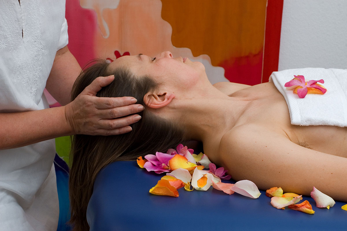 Therapist performing Lomi Lomi massage on a client lying among flower petals, focusing on the head and neck.