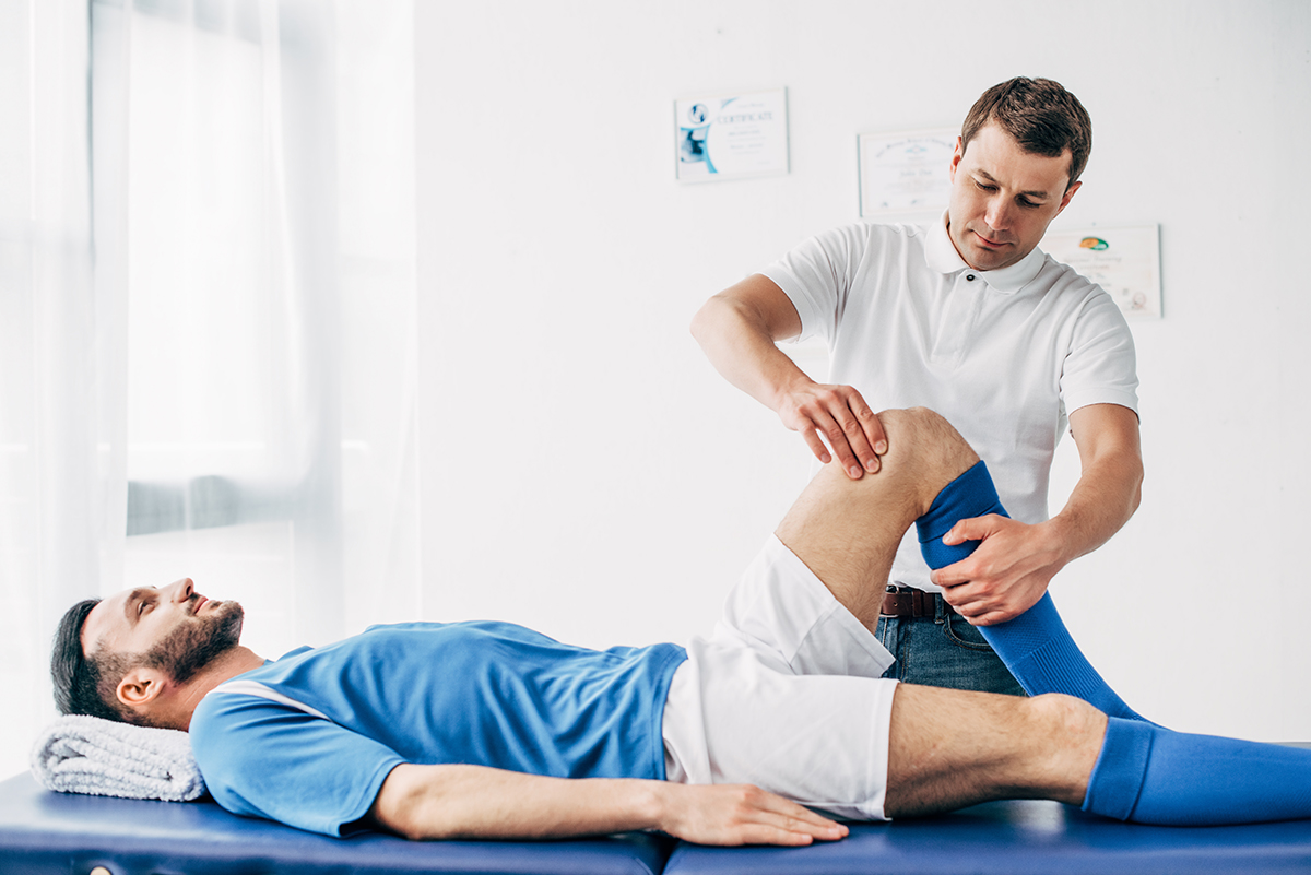 Sports therapist performing knee rehabilitation massage on male soccer player wearing blue uniform and socks
