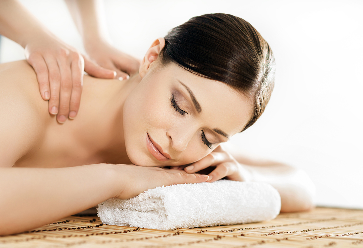 Woman lying on a massage table with eyes closed, resting her head on a folded white towel while receiving a relaxing Swedish back massage