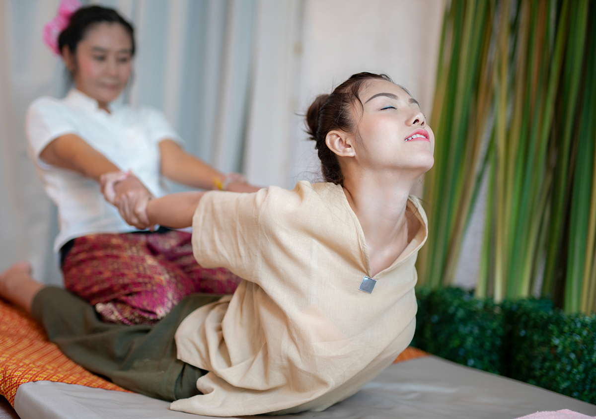 Therapist performing a traditional Thai massage, pulling the client’s arms back to assist with a deep chest and back stretch
