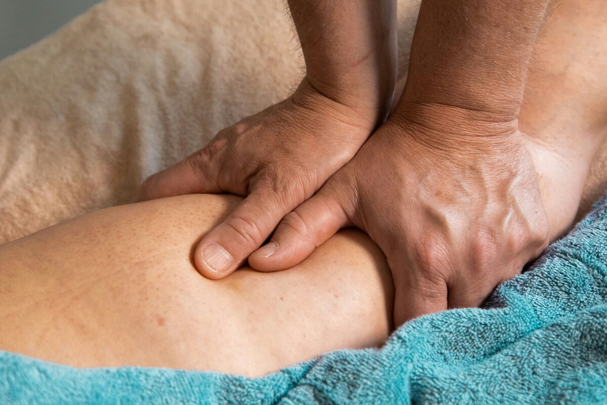 Therapist applying firm thumb pressure along a client’s upper arm while the client rests on a massage table.