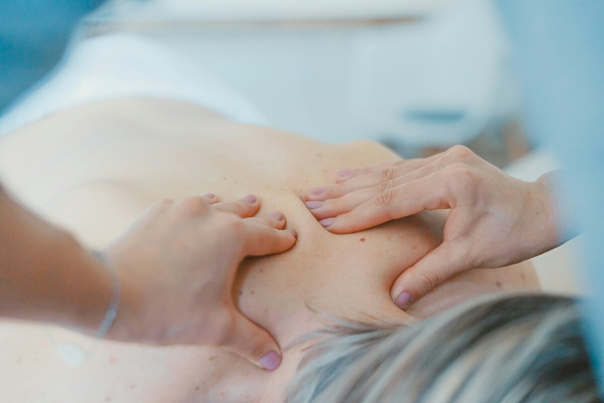 Therapist pressing into a client’s upper back muscles with both thumbs during a relaxation massage.