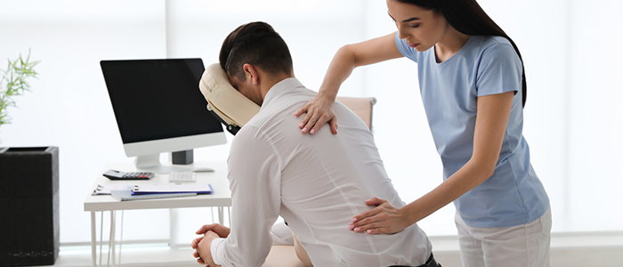 Male office worker receiving a back massage on a chair from a female therapist