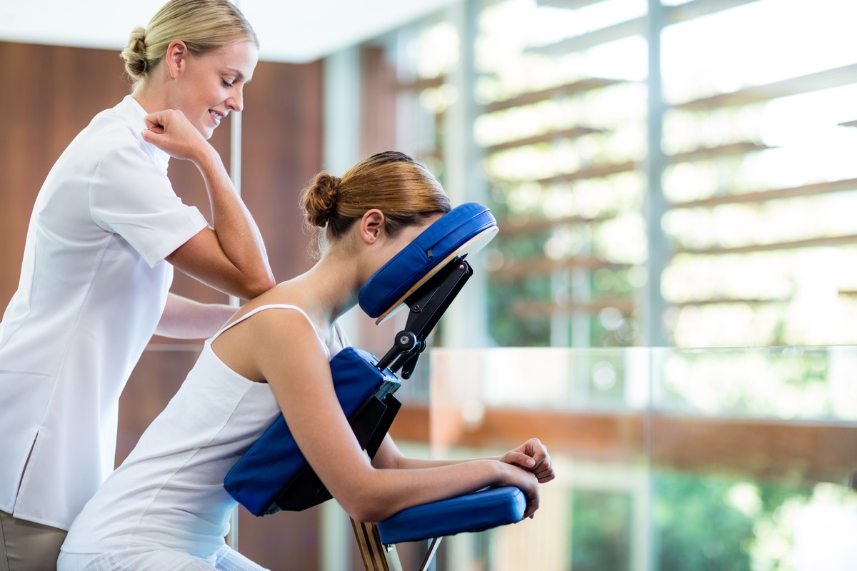 Chair massage therapist using elbow technique on client’s shoulders in workplace setting