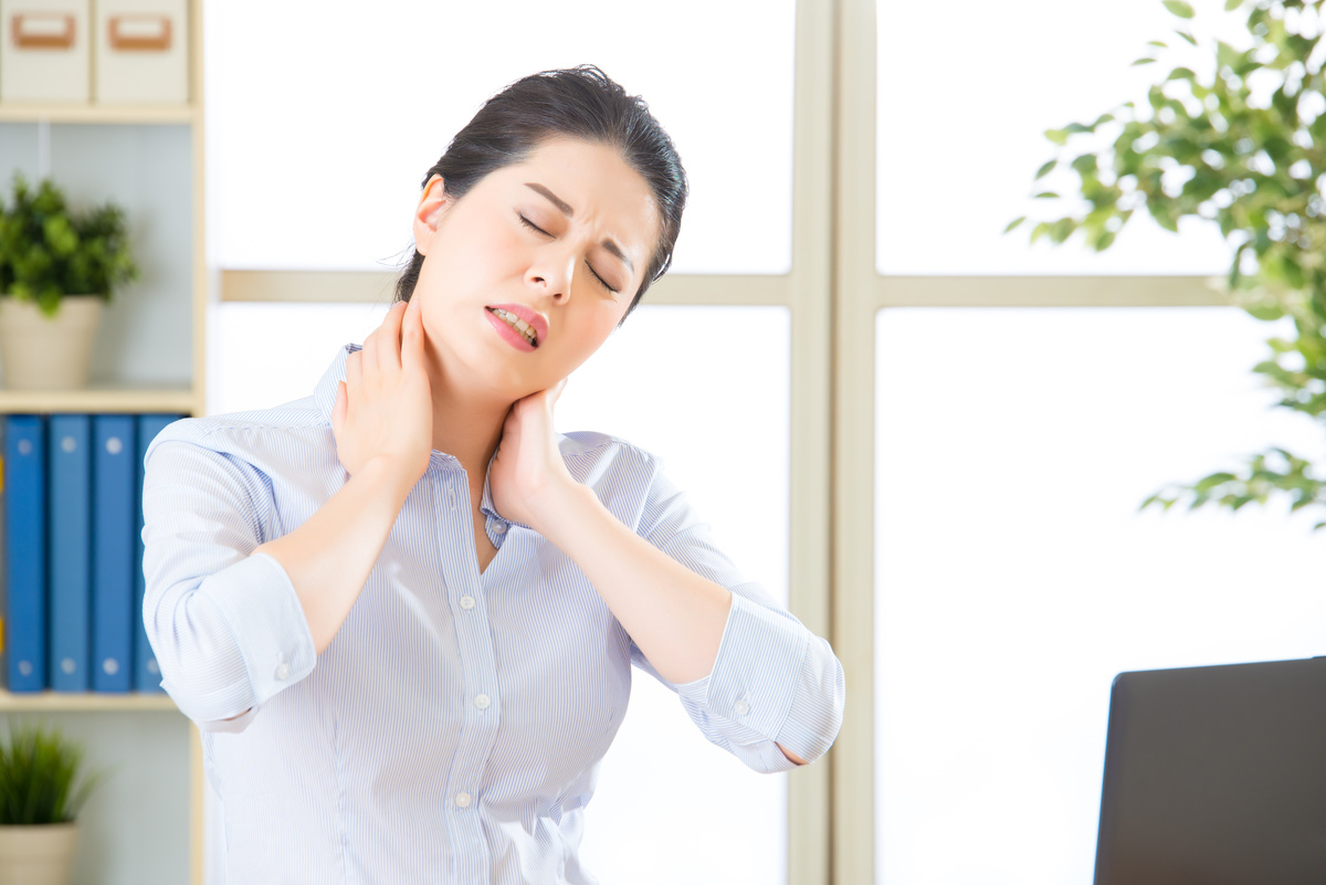 Female office worker holding her neck in pain while sitting at a desk