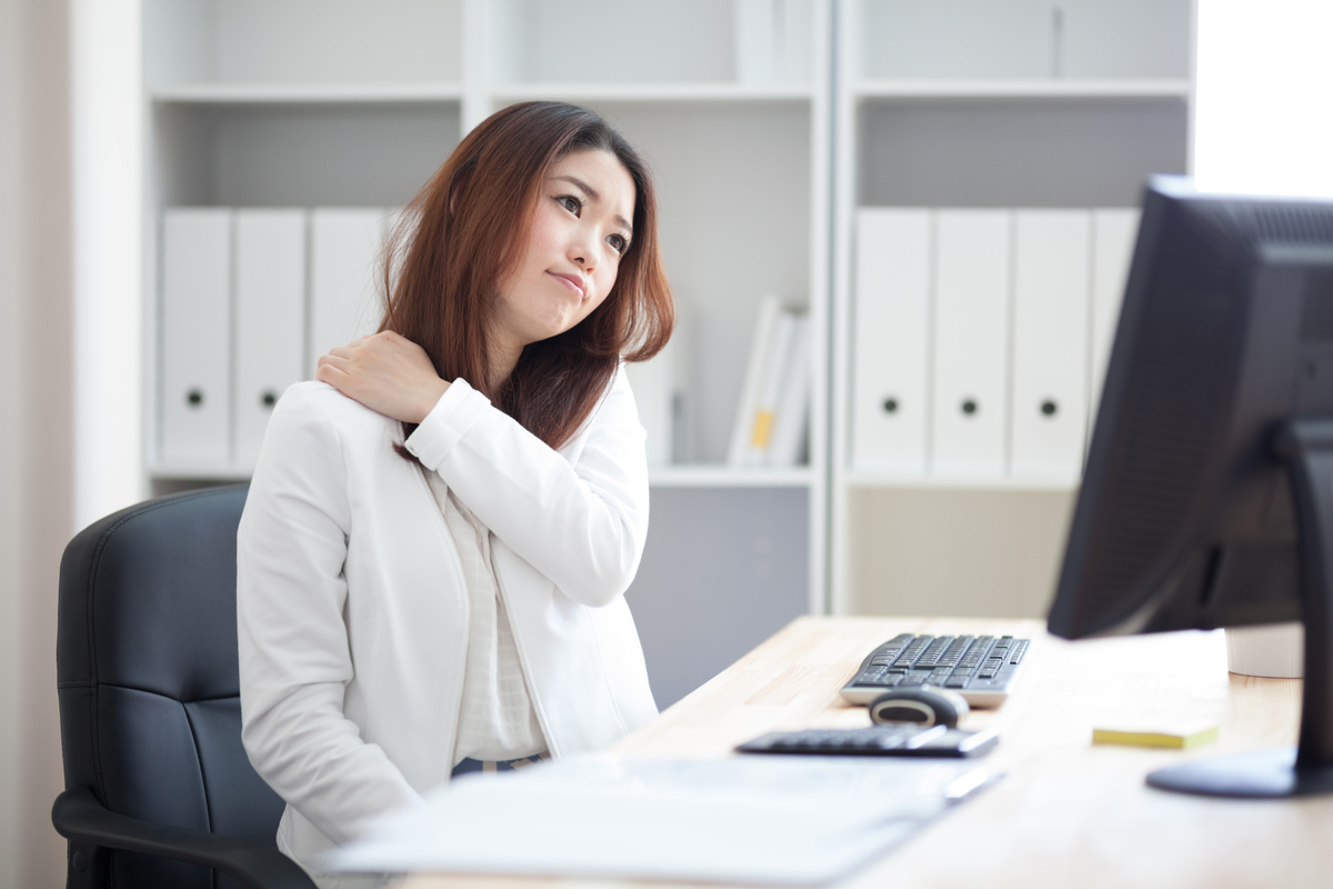 Female office worker holding her shoulder in pain while sitting at a desk