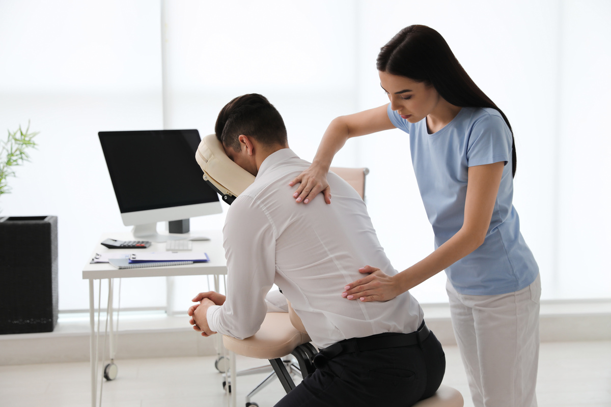 Female office worker receiving back massage in chair from female therapist in bright office
