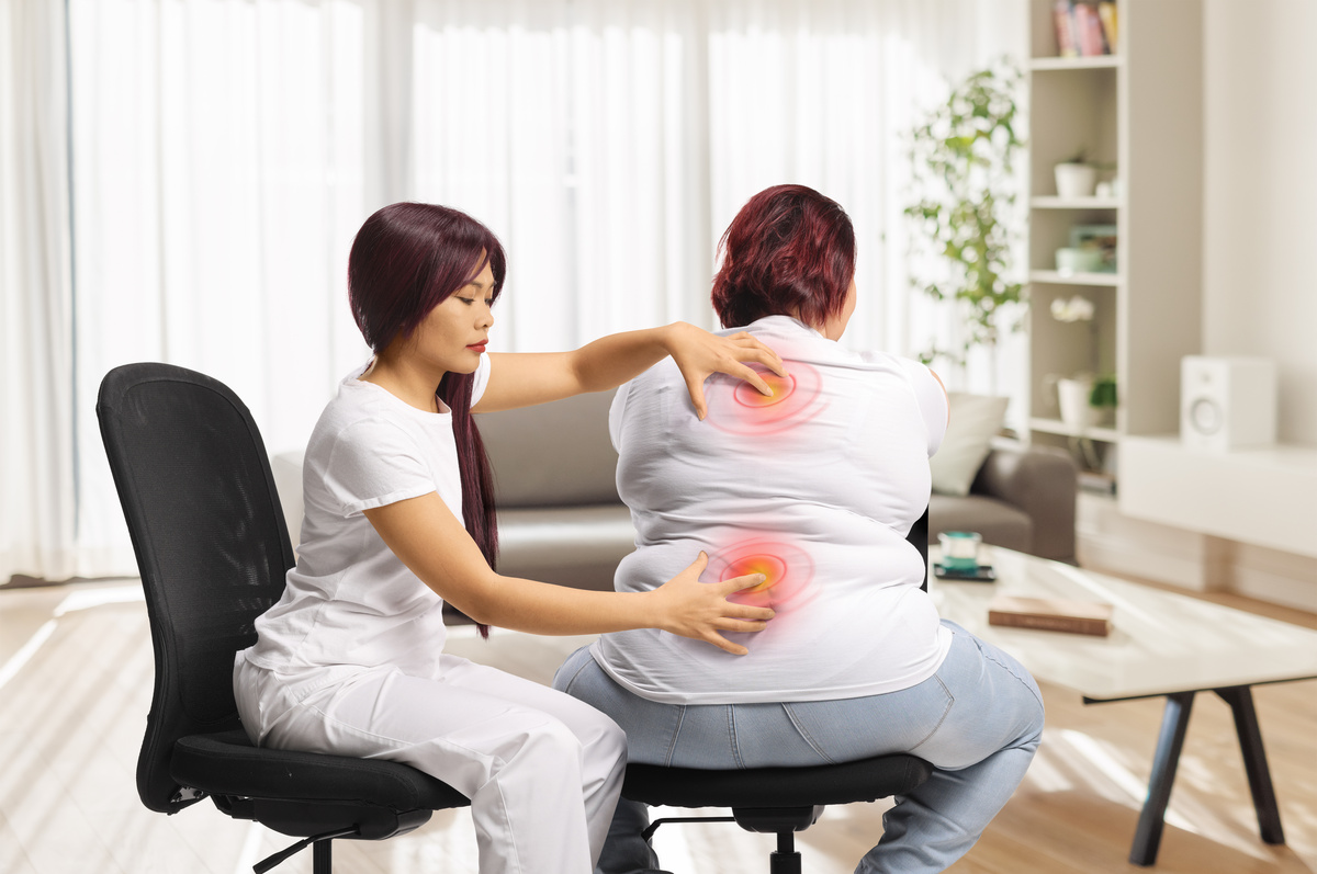 Female office worker relaxing in massage chair with therapist providing shoulder treatment