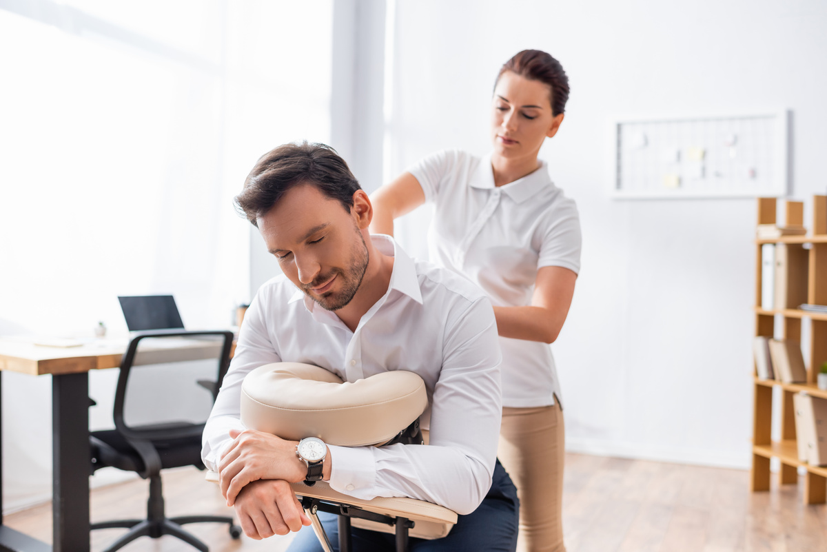 Female therapist applying shoulder pressure during chair massage in office