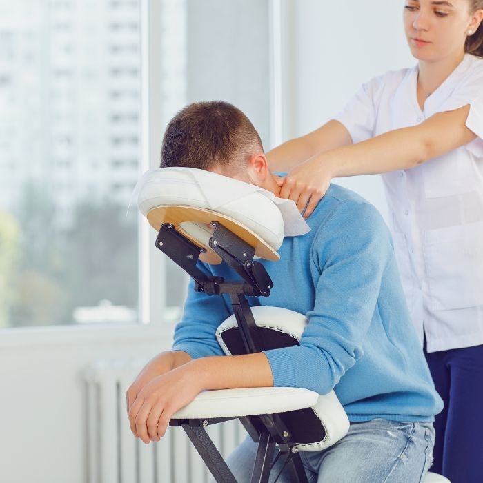 Male office worker receiving shoulder massage in chair at workplace