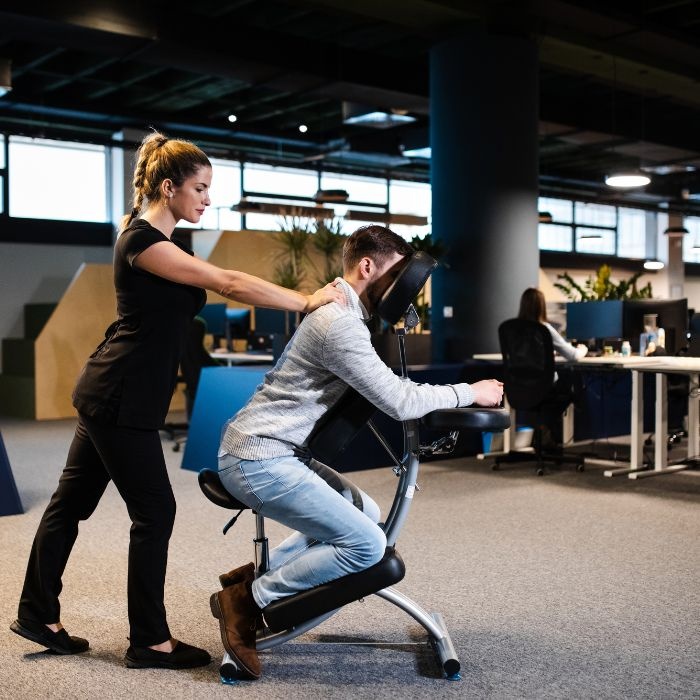 Therapist giving upper back massage to male office worker in a chair