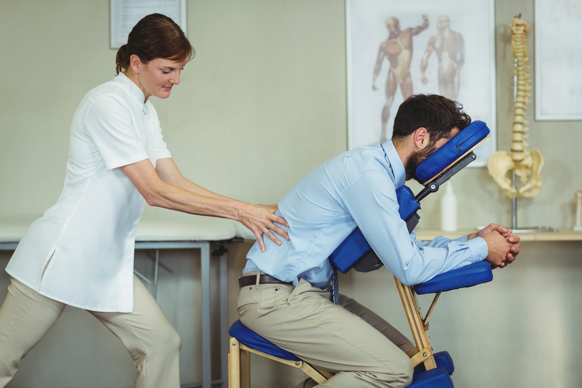 Female therapist applying pressure to a male office worker’s lower back during chair massage