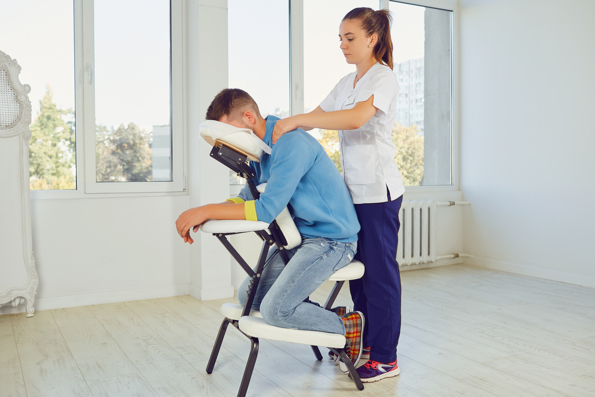 Female therapist massaging a male office worker’s neck and shoulders in a chair