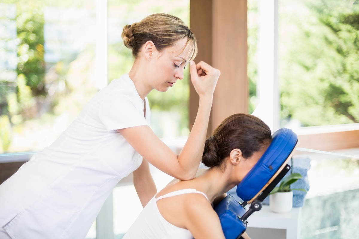 Female therapist applying forearm pressure to relieve tension in a client’s upper back