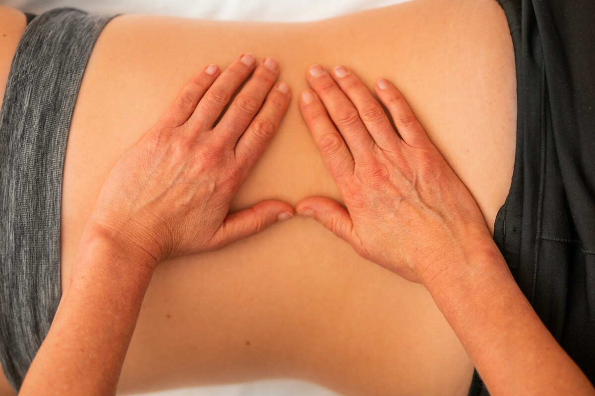 Close-up of therapist’s hands pressing deeply into the lumbar area of a client’s back.