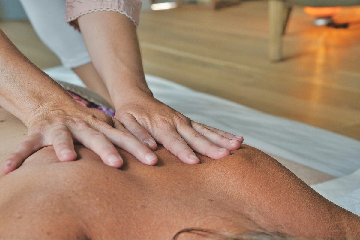 Therapist’s hands applying firm pressure to a client’s back in a bright massage studio.