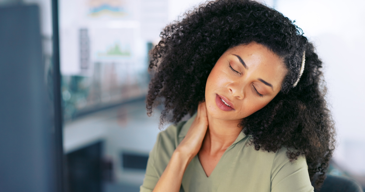 Office worker holding her neck in pain at desk, showing discomfort from workplace strain.