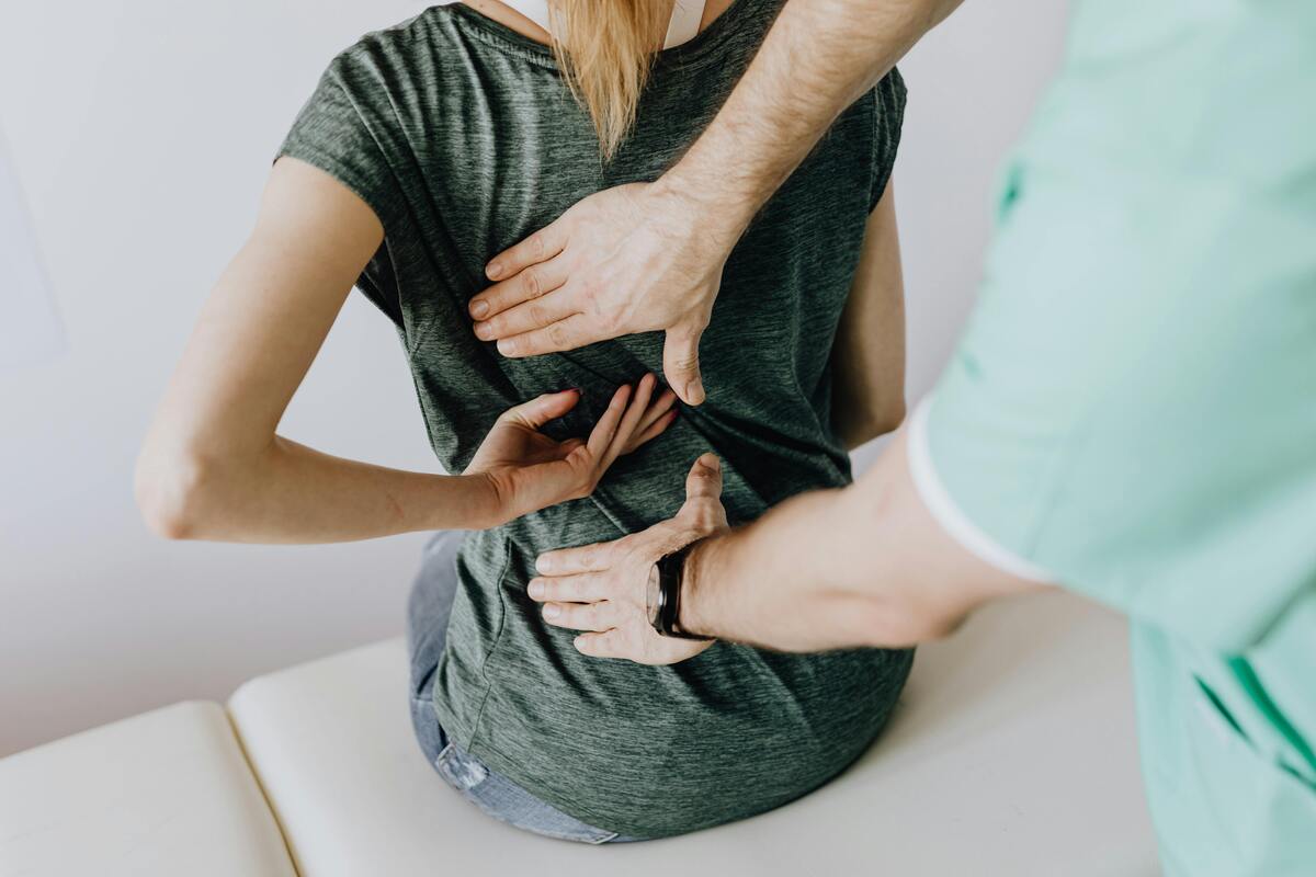 herapist guiding a seated woman’s back with hands-on adjustment for posture alignment and pain relief.