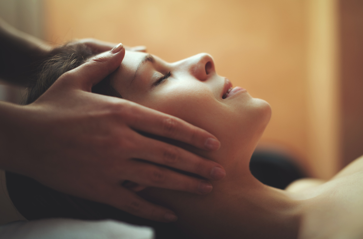 Woman lying with eyes closed as therapist gently massages her temples and scalp.