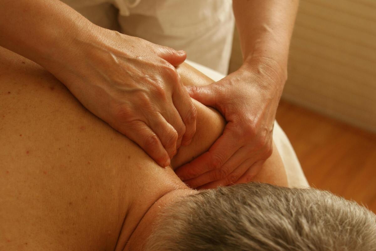 Therapist applying firm pressure to an older man’s shoulder during a therapeutic massage.
