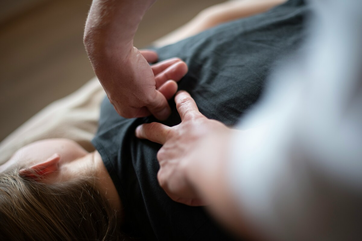 Therapist applying thumb pressure to a shoulder trigger point while client lies face down.