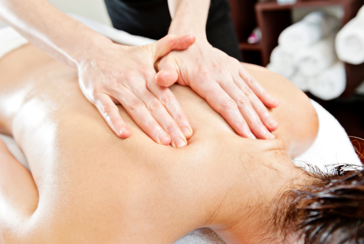 Close-up of hands performing Swedish massage strokes on a client’s back.