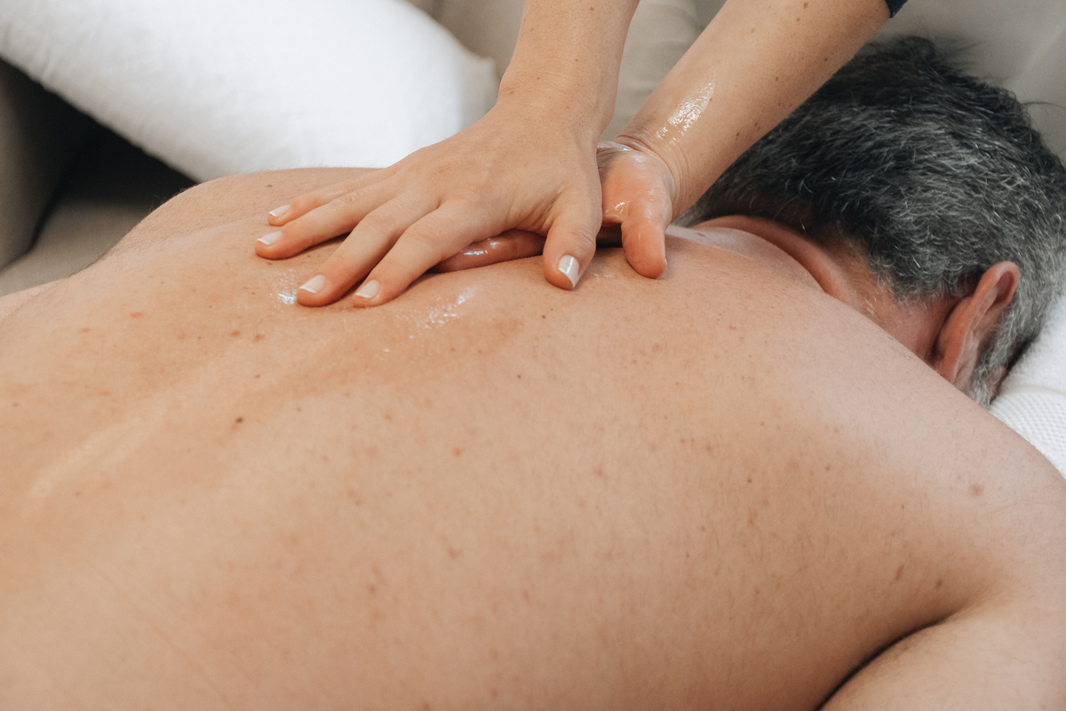 Therapist applying oil and performing a Swedish massage stroke across a client’s back in an at-home setting.