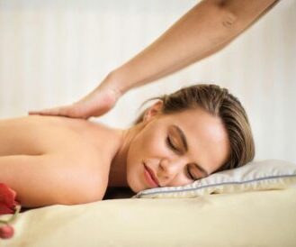 Woman smiling peacefully while receiving a Swedish back massage, lying on a spa table with flowers nearby.